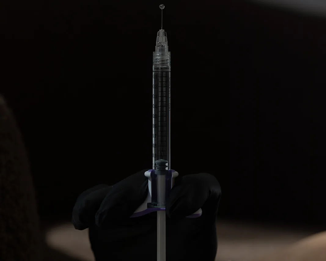 A dermal filler syringe held in an editorial still at MODE.
