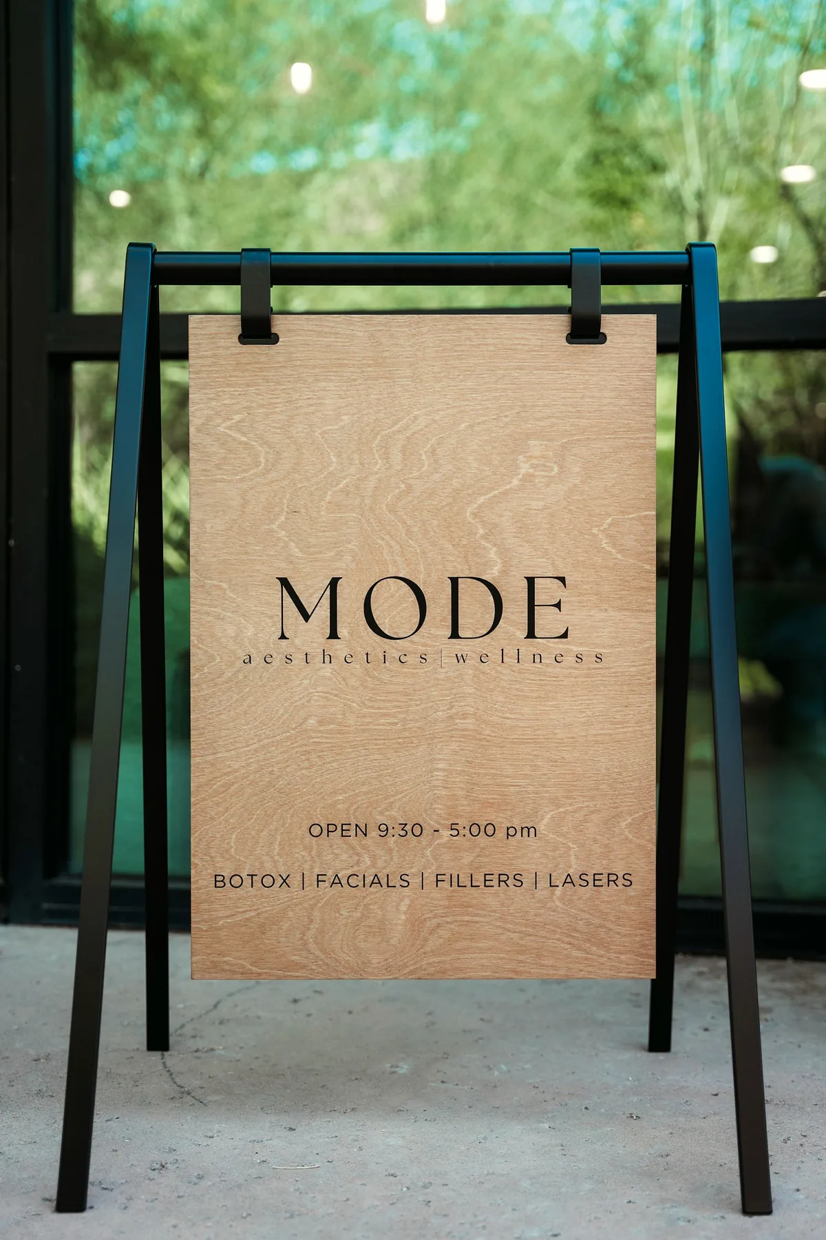 The MODE Aesthetics and Wellness sidewalk sign outside the practice on E Pinnacle Peak Road in North Scottsdale, Arizona, listing weekday hours of 9:30am to 5pm